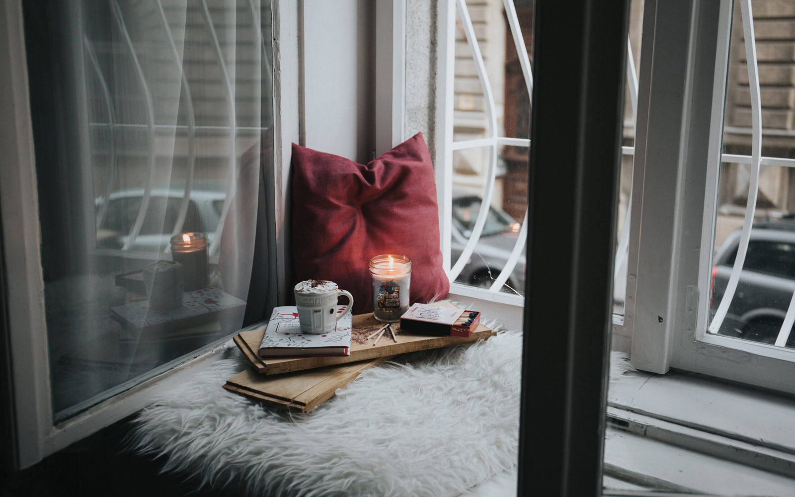 Cozy window nook with candle, books, and hot drink.