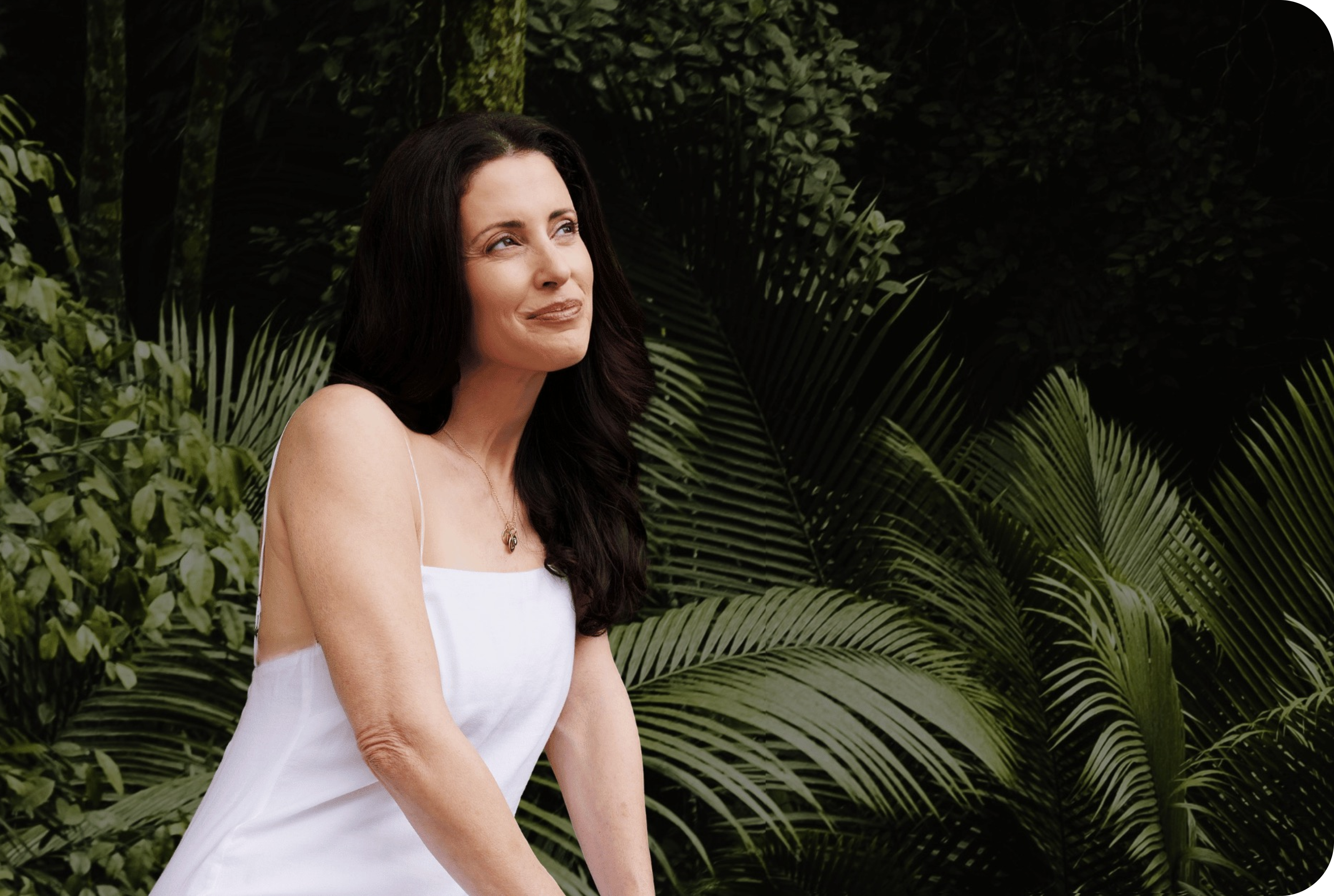 Woman smiling outdoor, tropical foliage background.