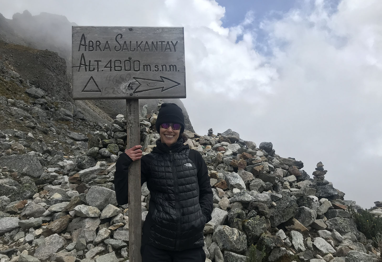 Hiker at Abra Salkantay sign on rocky trail.